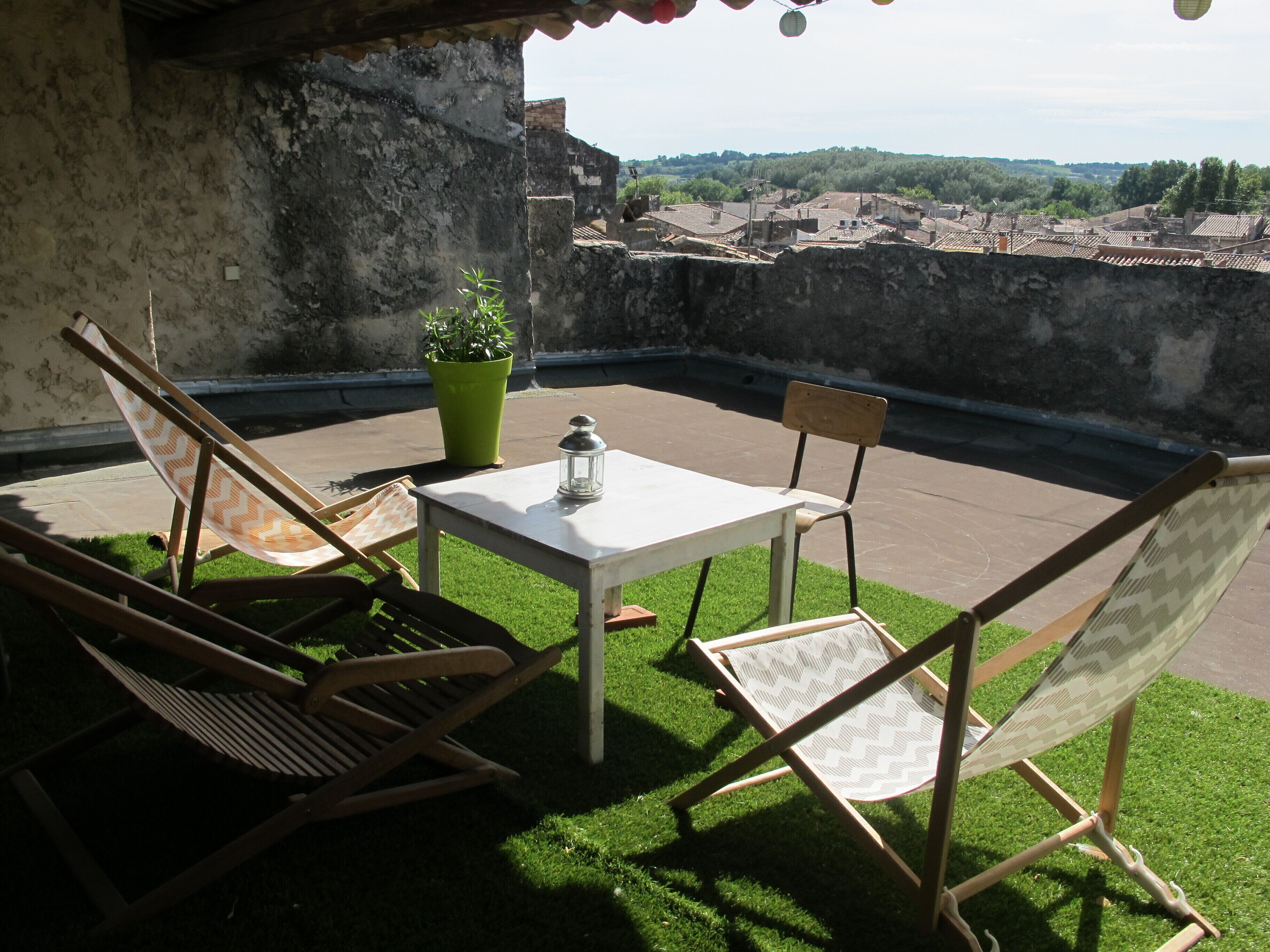 A rooftop terrace with a table and four chairs, a potted plant, and a lantern.