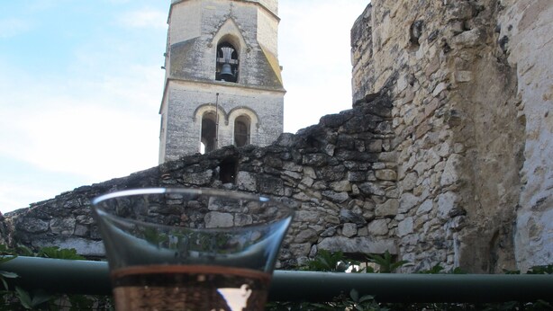 Un verre de vin sur une table en bois, avec un mur de pierre et une tour en arrière-plan.