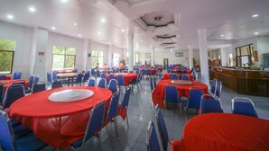 A large dining hall with round tables covered in red tablecloths and blue chairs.