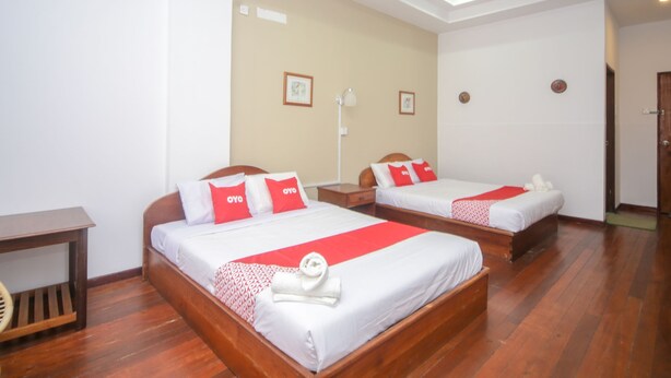 A hotel room with two beds, each with red and white bedding, wooden headboards, and a small bedside table.