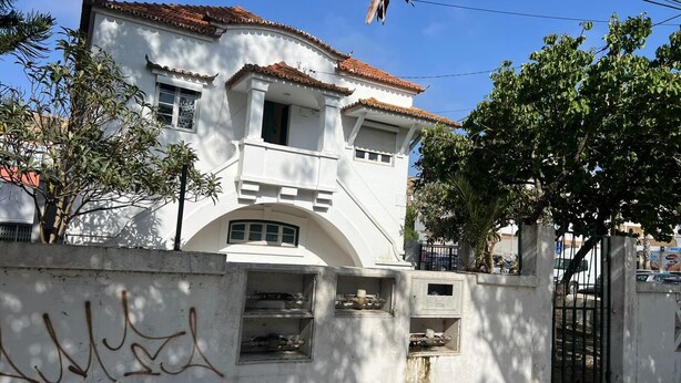 A white building with a tiled roof, a gated entrance, and a small balcony. - Come Inn Costa da Caparica (Almada)