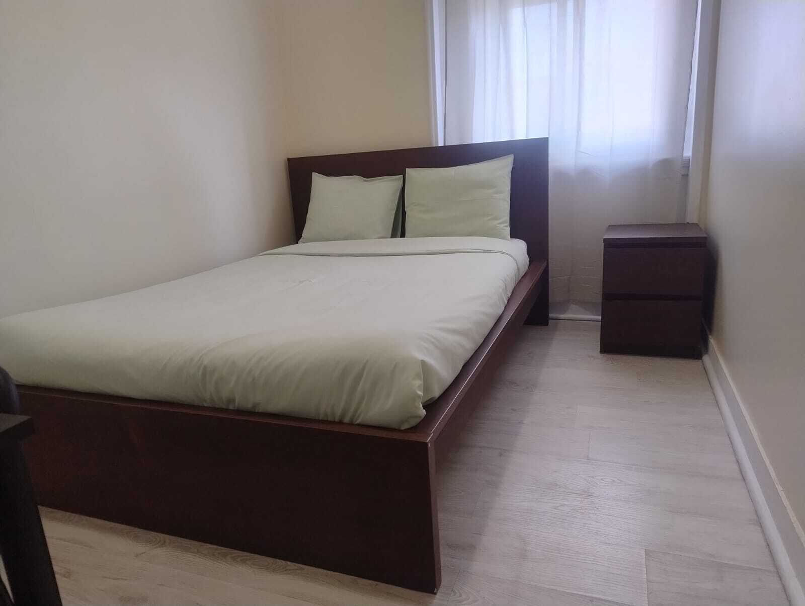 A bedroom with a bed, a nightstand, and a window with curtains.
