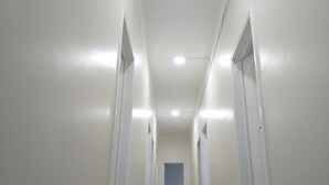 A narrow hallway with white walls and doors on both sides, leading to a room at the end. - Come Inn Costa da Caparica (Almada)