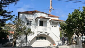 A white building with a tiled roof, a balcony, and a small arched entrance. - Come Inn Costa da Caparica (Almada)
