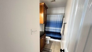 A compact bathroom with a toilet, wooden cabinets, a shower curtain, and a tiled floor.