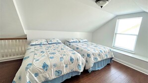A bedroom with two beds, a sloped ceiling, a window, and a radiator.