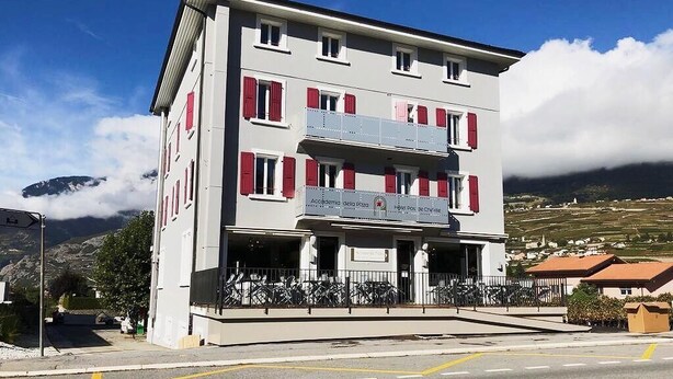 Un hotel de varios pisos con balcones, una señal que indica que es un hotel y montañas al fondo.