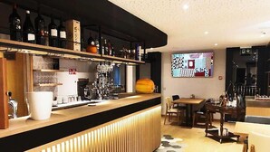 Un área de bar moderna con mostrador de madera, estantes con botellas y una zona de estar con mesas y sillas.