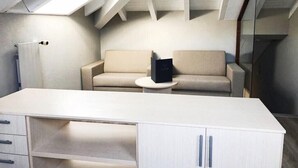 Una habitación moderna y minimalista con un escritorio blanco, un sofá color beige y una pequeña mesa redonda.