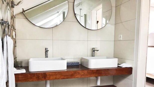A bathroom with two sinks, wooden shelves, and two round mirrors. - Hotel Pas de Cheville (Conthey)