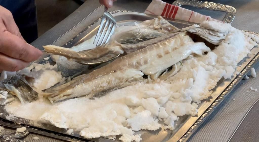 Une personne utilise une pince pour manipuler du poisson sur un plateau.