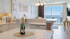A modern kitchen with a view of the sea, a dining area with a table, and a bar area with a bottle of champagne. - Majestic T2-1606 - Fabulous Three Bedrooms Condo! (Panama City Beach)