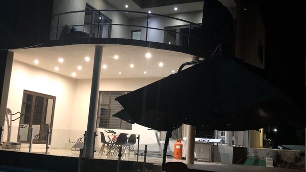 An outdoor pool area with a dining table and chairs, a covered seating area, and a modern building in the background. - Naldorado Executive Villa (Mbombela)