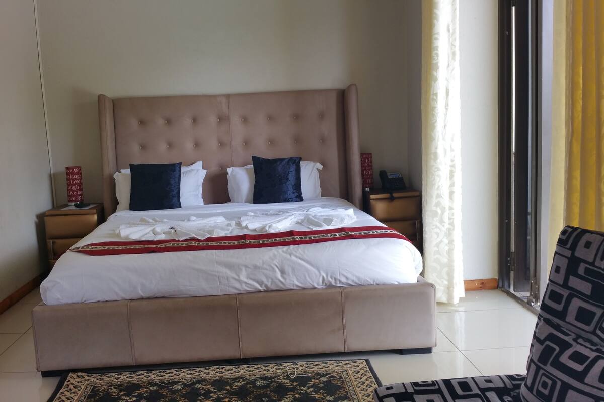 A neatly made bed with a red and gold decorative trim, a tufted headboard, and a bedside table with a telephone.
