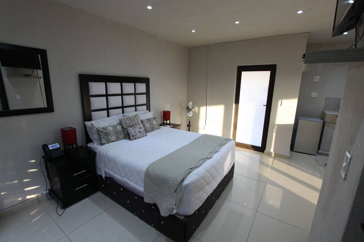 A modern bedroom with a large bed, bedside tables, a mirror, and a sliding door to a bathroom.