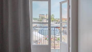 A room with a large sliding glass door leading to a balcony with a view of a marina and buildings.
