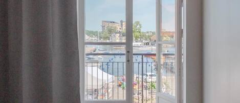 A room with a large sliding glass door leading to a balcony with a view of a marina and buildings.