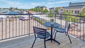 A wooden deck with two black metal chairs and a small round table, overlooking a marina with boats and buildings. - Hamnhotellet (Vastervik)