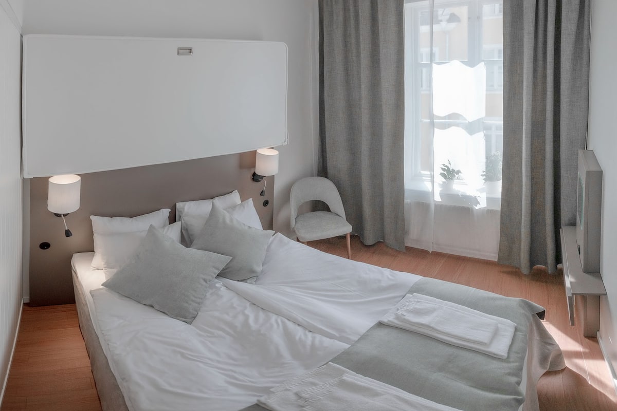 A hotel room with a bed, a chair, a TV, and a window with curtains.