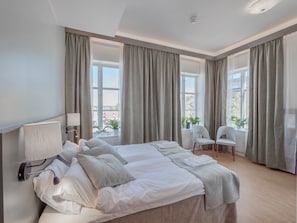 A modern hotel room with a large bed, two chairs, a window with curtains, and a view of the city. - Hamnhotellet (Vastervik)