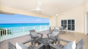 A balcony with a view of the ocean, a table with chairs, and ceiling fans. - Laguna Del Mar (Seven Mile Beach)