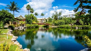 A resort with a large pond, palm trees, and a bridge. - Laguna Del Mar (Seven Mile Beach)