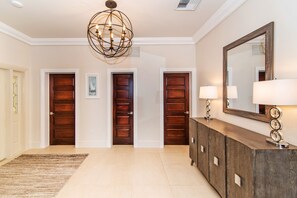 Un pasillo espacioso con tres puertas de madera, un espejo grande y una lámpara de araña moderna.