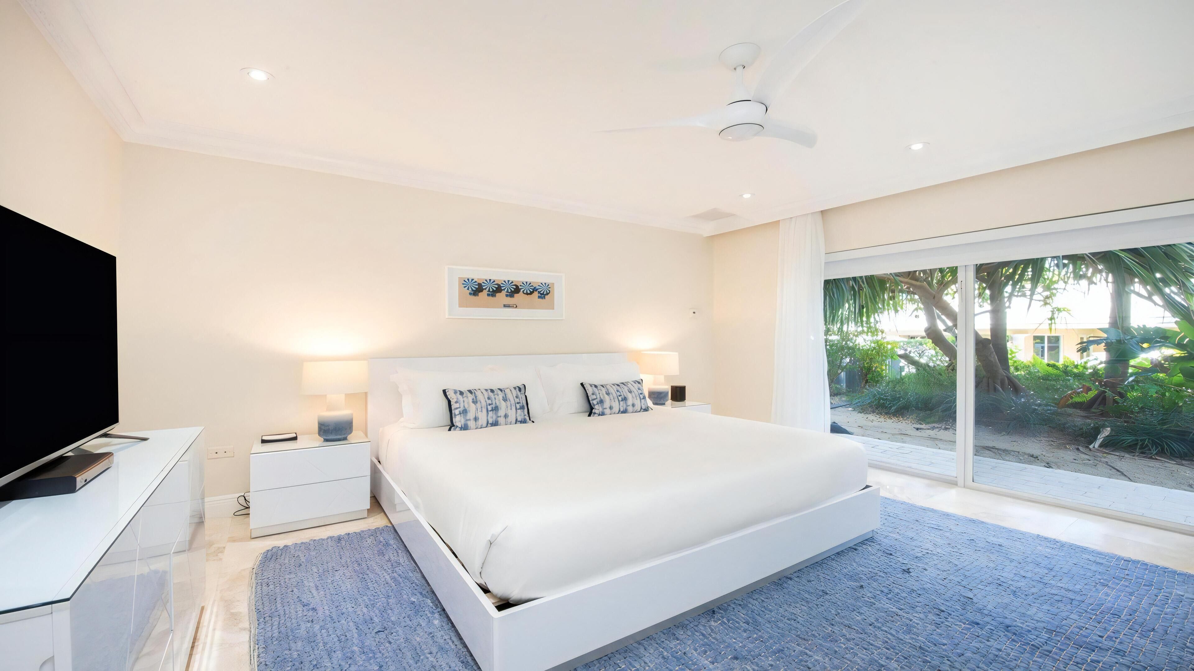 Un dormitorio moderno con una cama grande, un televisor de pantalla plana y vistas a un jardín a través de una puerta corrediza de vidrio.
