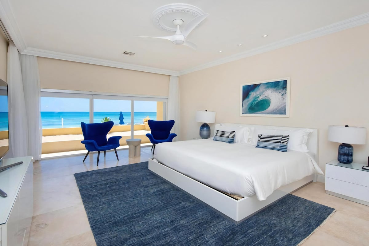 Ein Schlafzimmer mit einem großen Bett, einem Schreibtisch, einem Sessel, einem Deckenventilator und Blick auf den Strand.