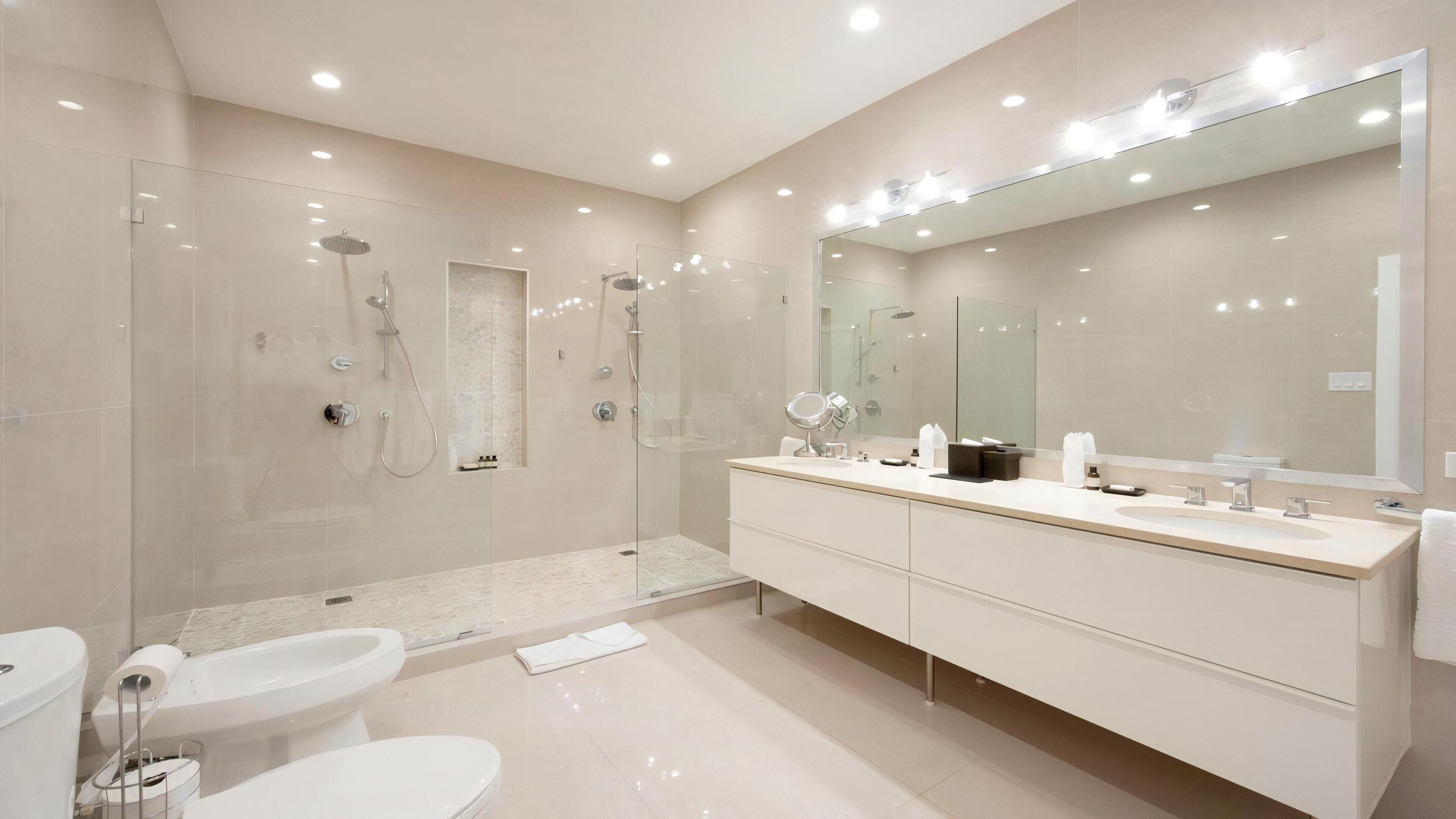 Een moderne badkamer met een douchecabine van glas, een grote spiegel en een wit wastafelmeubel.