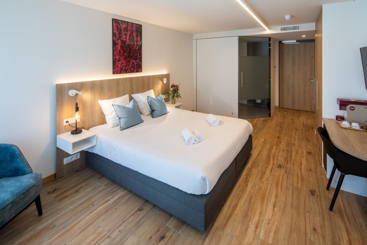 A modern hotel room with a large bed, bedside table, and a desk area.