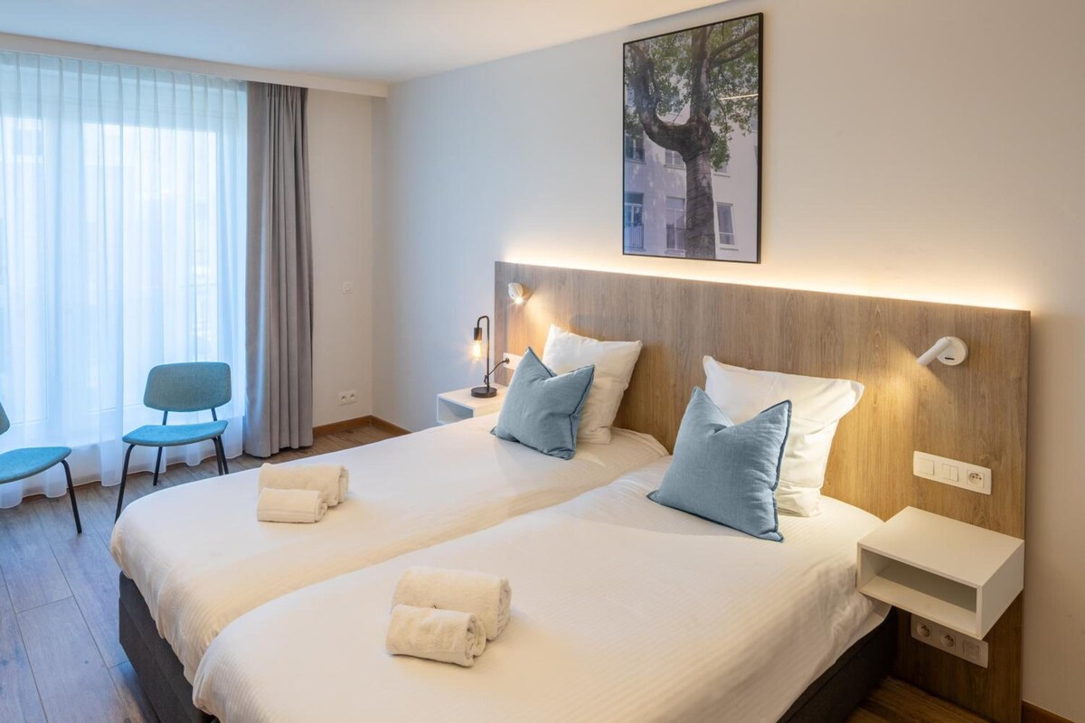 A hotel room with two beds, a desk, a chair, and a window with curtains.