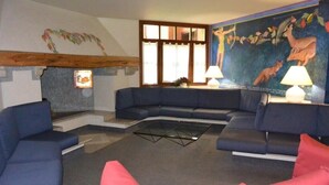 A living room with a blue sectional sofa, a glass coffee table, and a mural on the wall. - Residence Rio Falzè ~ TWO-ROOM APARTMENT TYPE A1 # 28 (Campo Carlo Magno)
