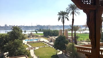 Vista de un patio con piscina, palmeras y un río al fondo.