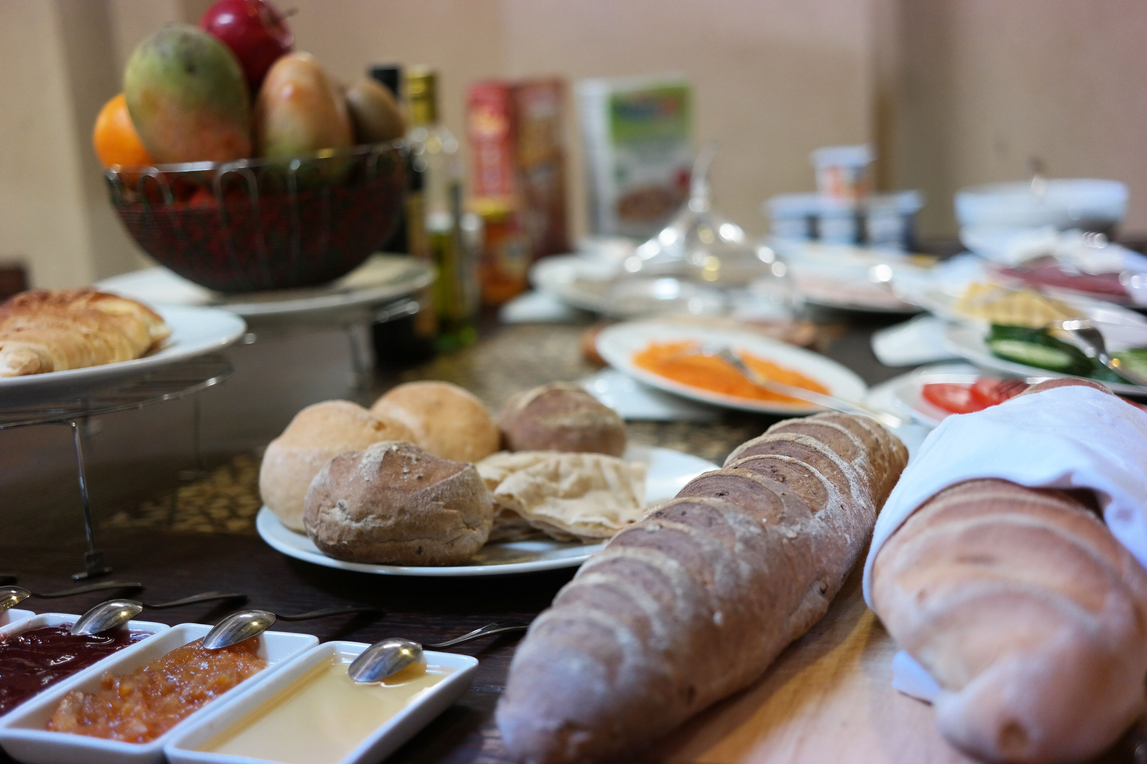 A buffet table with various food items including bread, pastries, and condiments.