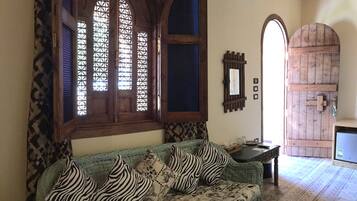A cozy room with a woven sofa, patterned cushions, a wooden door, and a mirror on the wall.