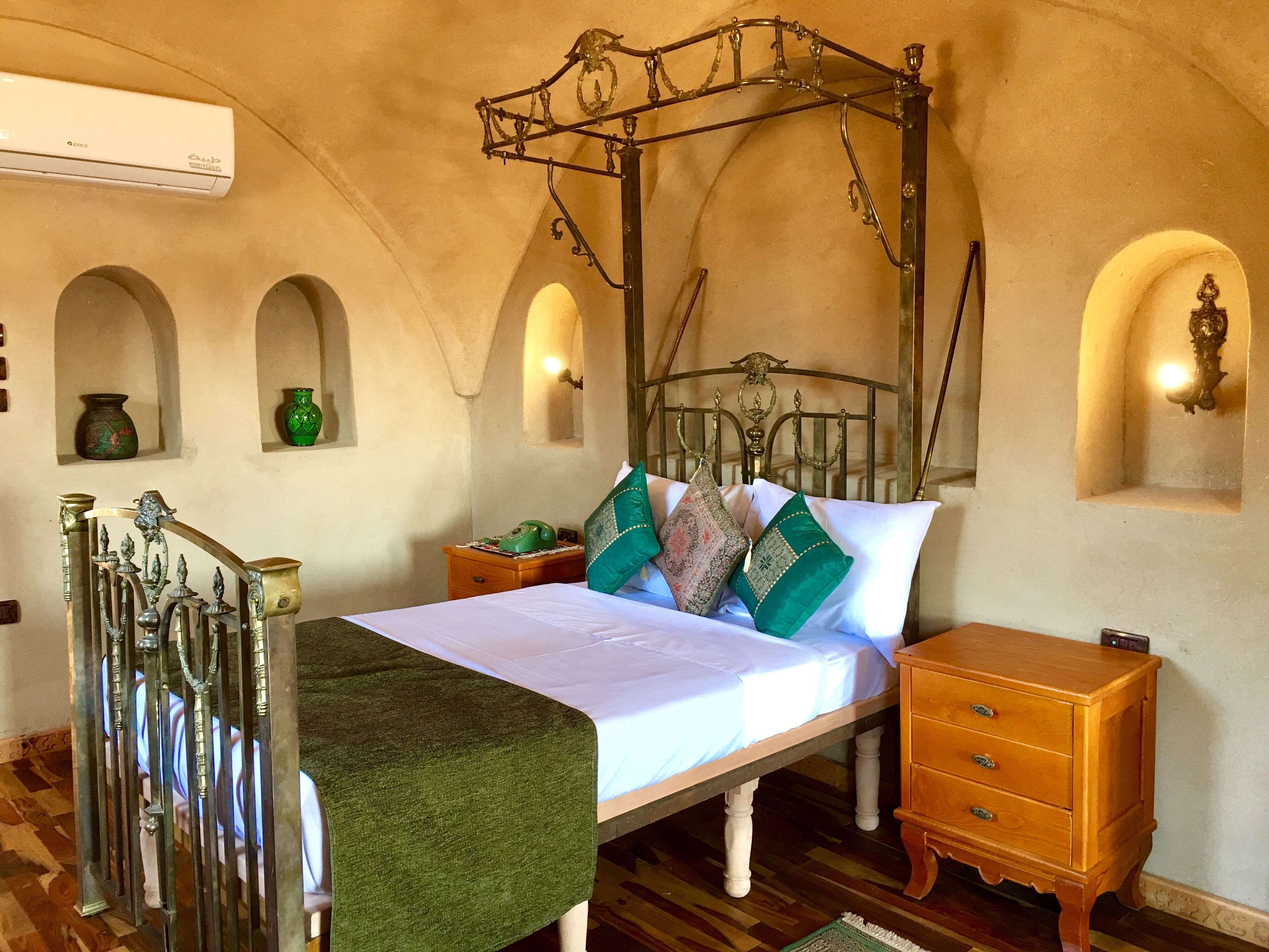 Une chambre à coucher avec un lit à baldaquin, une table de chevet en bois, un plaid vert et un climatiseur fixé au mur.