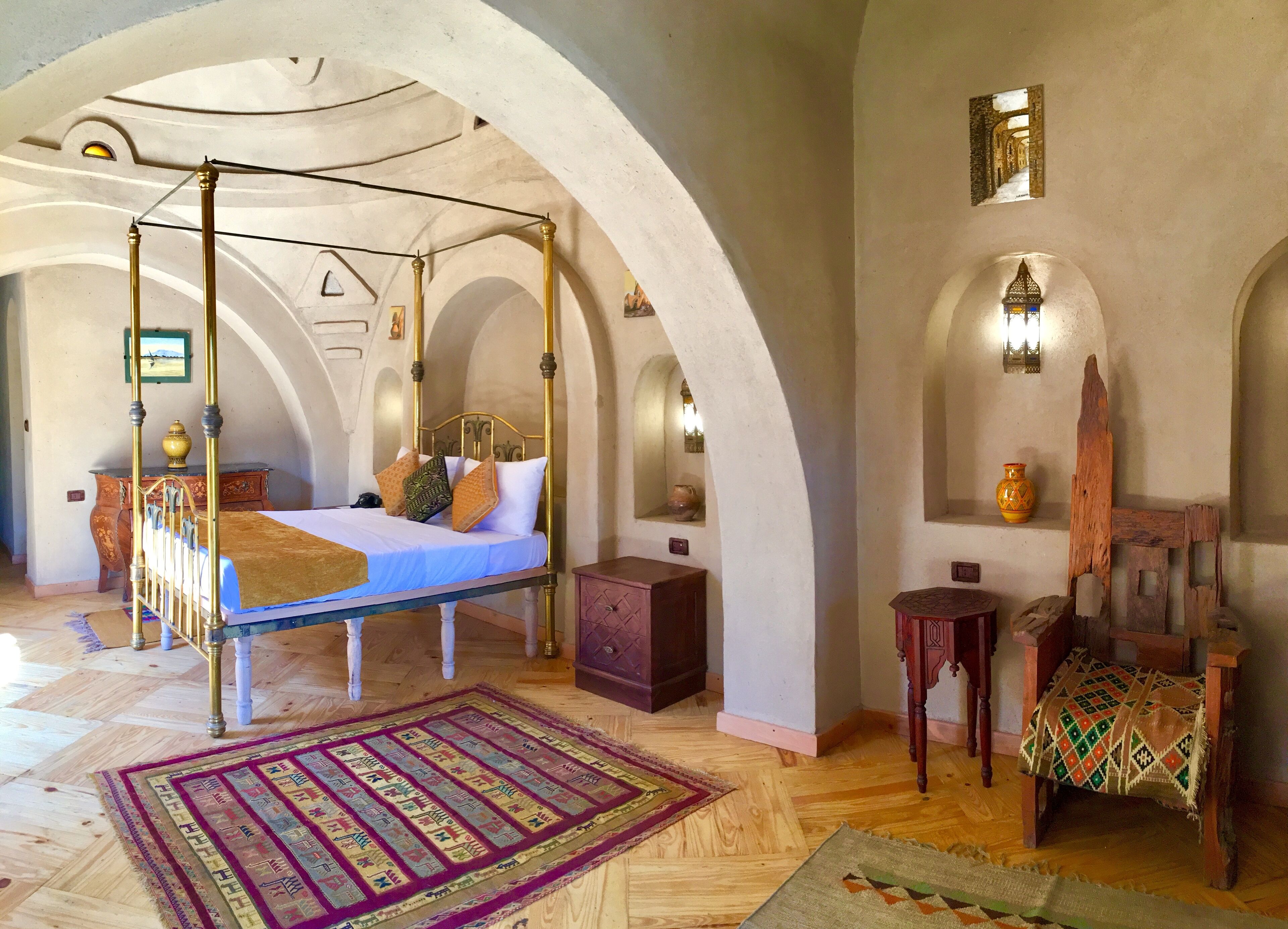 A four-poster bed with a blue bedspread, a patterned rug, and a wooden chair with a cushion.