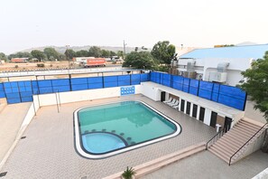 A swimming pool with a hot tub, surrounded by a blue fence, and a staircase leading to a building with air conditioning units.