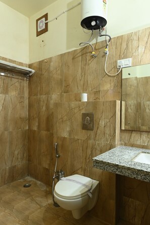 A bathroom with a marble floor, a toilet, a shower with a handheld showerhead, and a sink with a granite countertop.