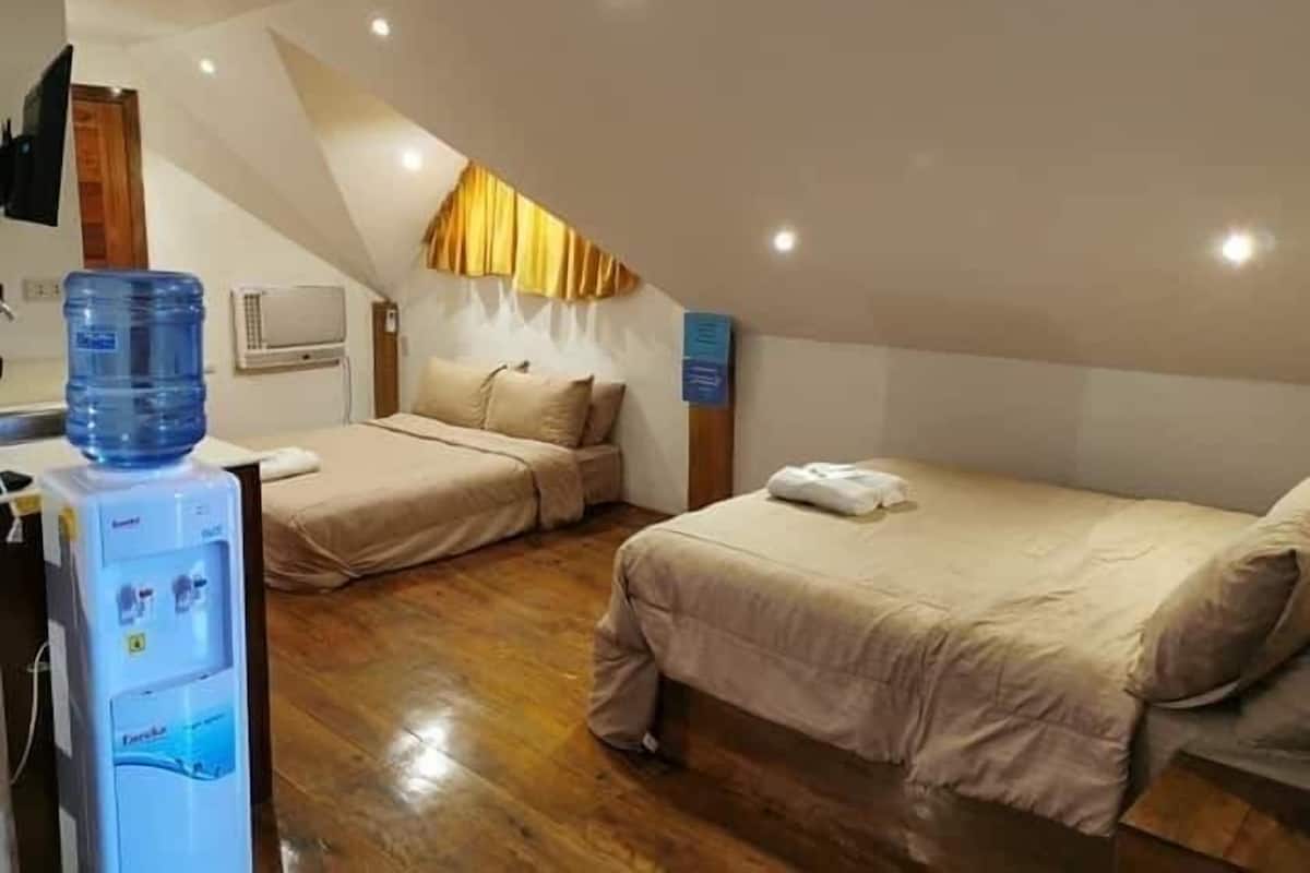 A hotel room with two beds, a water dispenser, and a ceiling fan.