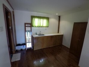 A small kitchen with wooden cabinets, a sink, and a window with green curtains.