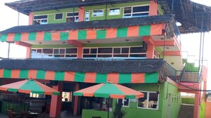 Een meerhoog gebouw met een groen en oranje gevel, zitplaatsen buiten met parasols, en een betegeld terras.