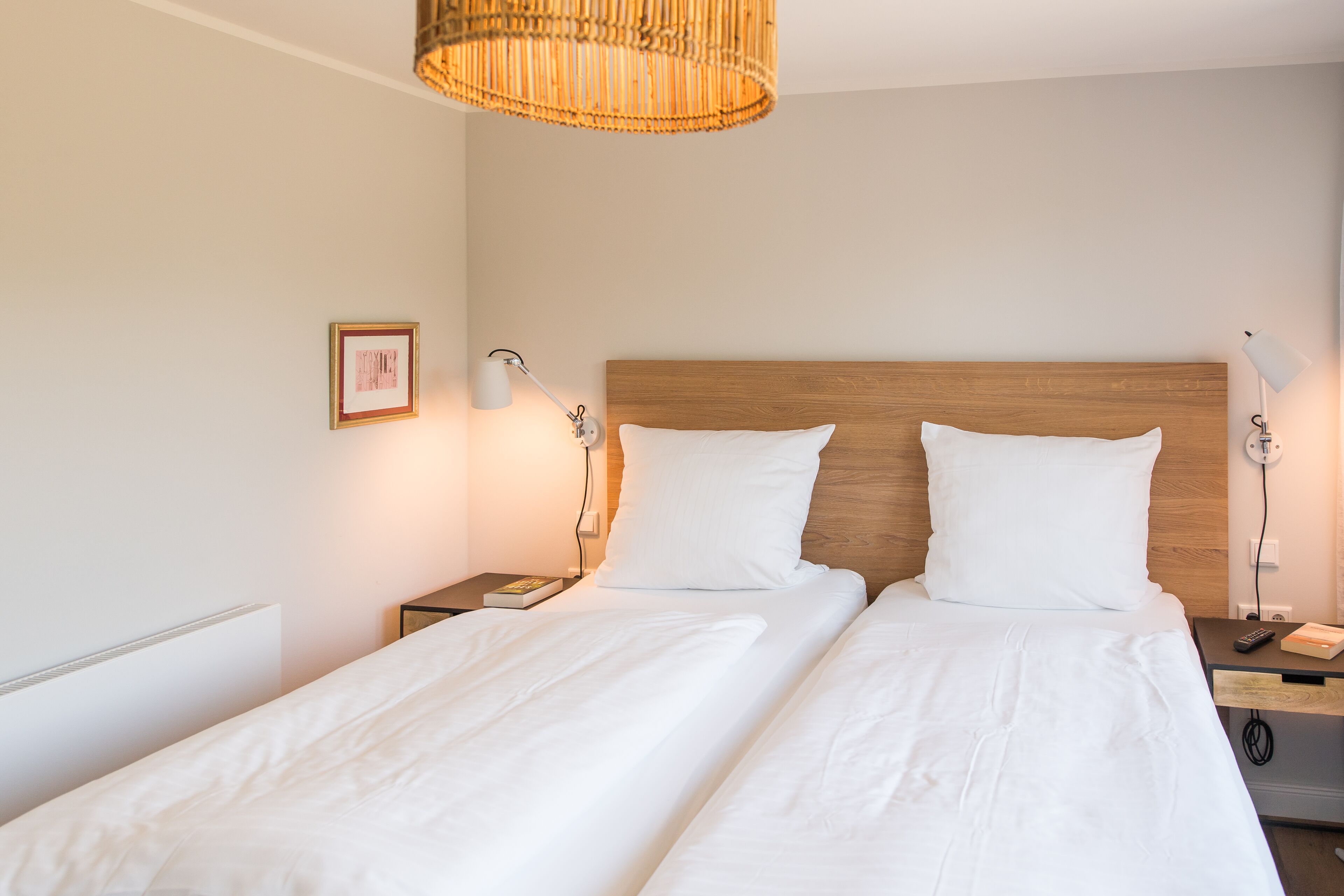 Habitación de hotel con dos camas individuales, mesitas de noche con lámparas, cabecera de madera y una lámpara colgante.