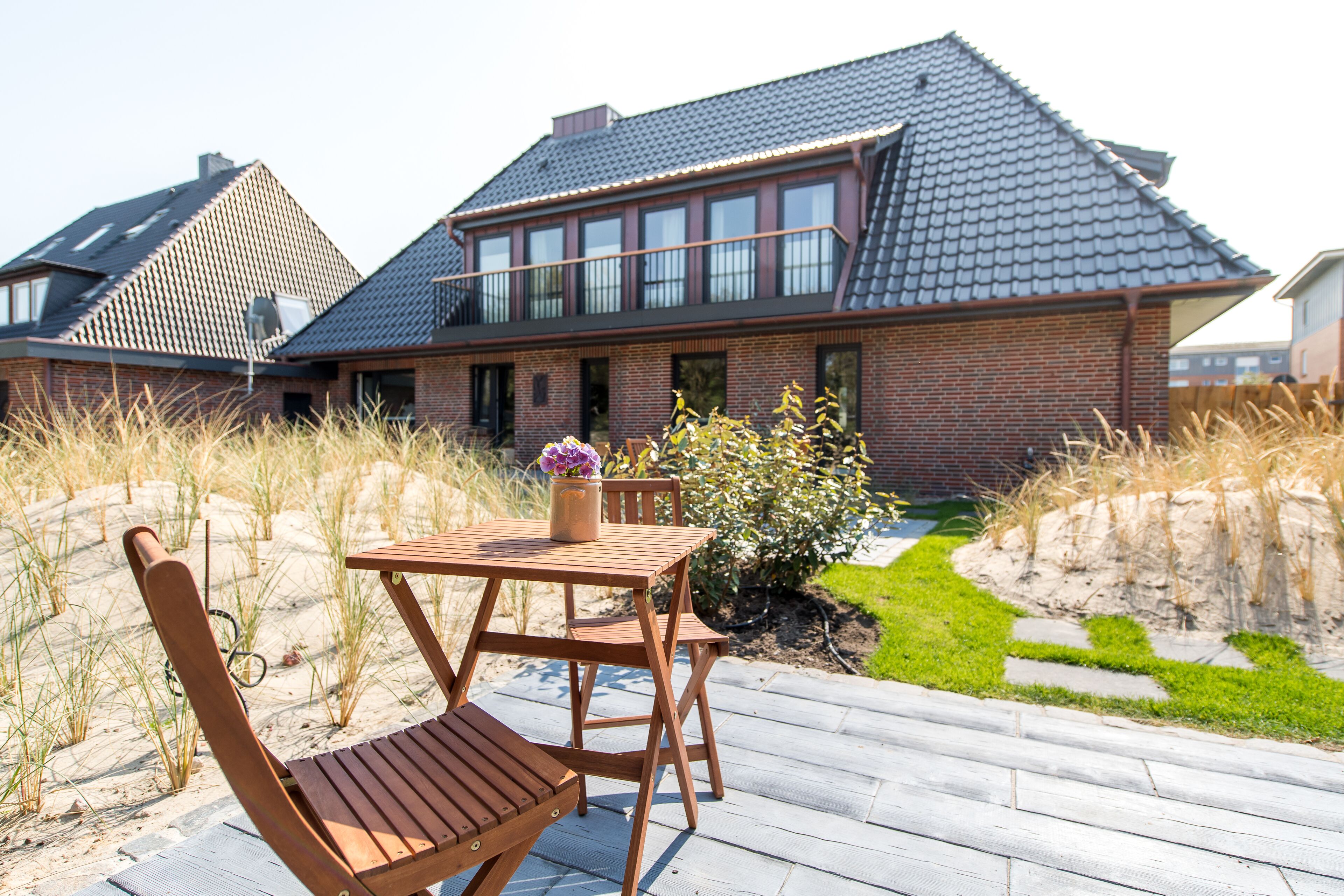 Une maison moderne dotée d’une grande terrasse, d’un coin repas avec une table et des chaises, et d’un jardin bien entretenu.