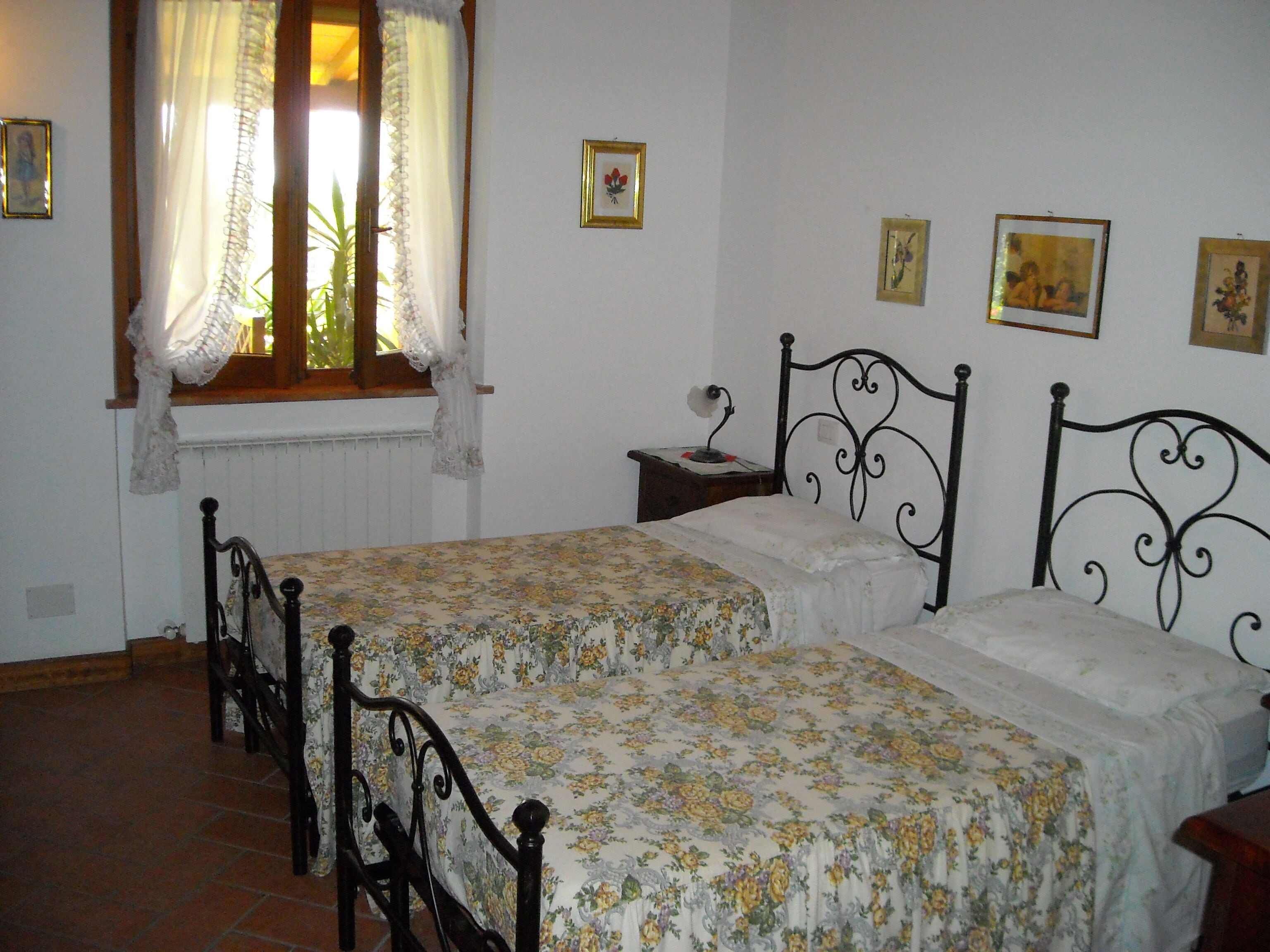 A bedroom with two beds, a window with curtains, and several framed pictures on the wall.