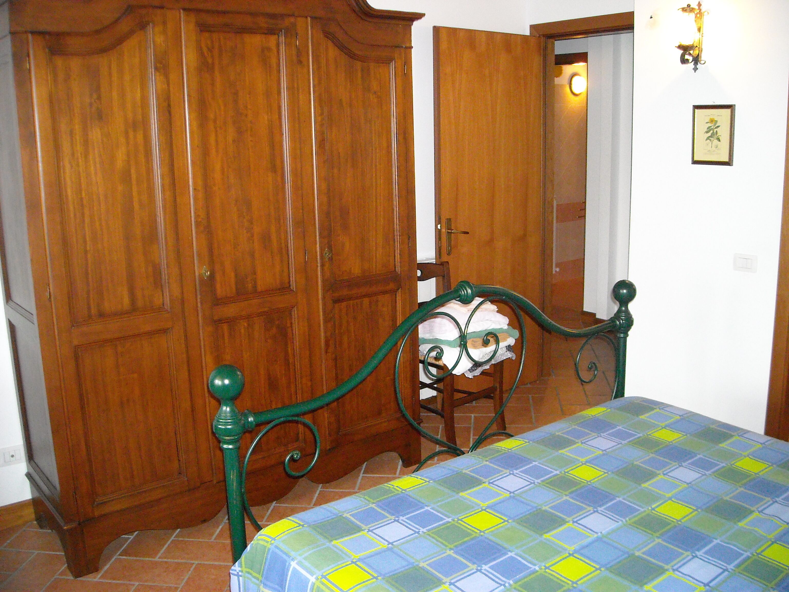 A bedroom with a bed, wooden wardrobe, and a door leading to another room.