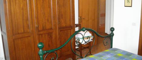 A bedroom with a bed, wooden wardrobe, and a door leading to another room.