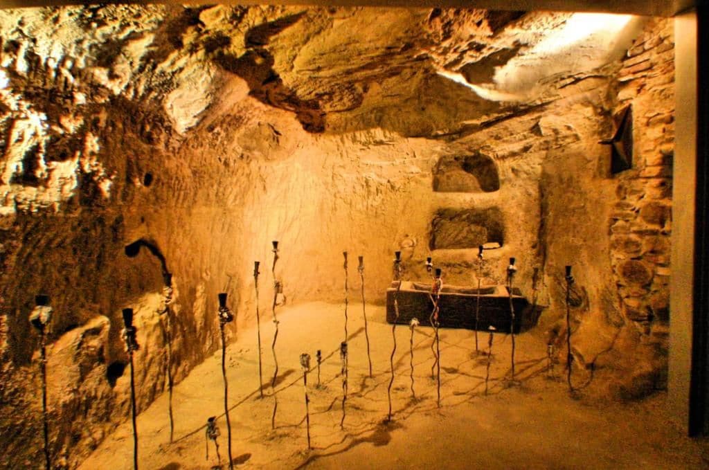 A cave-like interior with a central stone bench and multiple standing lamps.