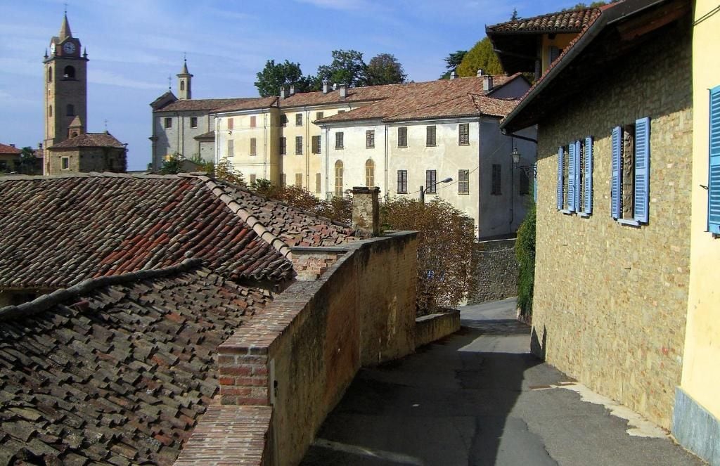 Ein schmaler Gang mit einer Backsteinmauer an einer Seite und einem Gebäude mit blauen Fensterläden an der anderen.